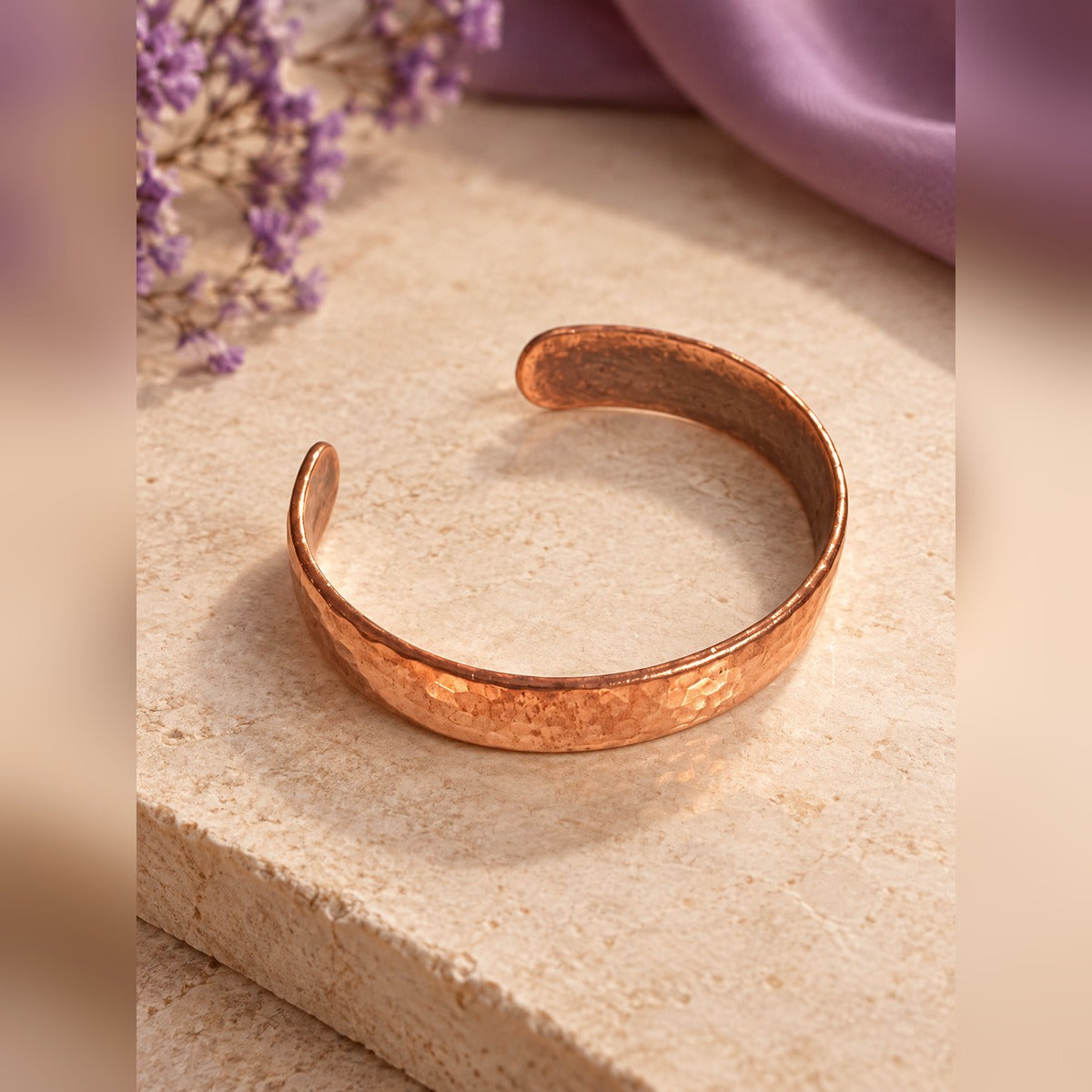 Hammered copper-tone open cuff bracelet with textured finish, on a stone surface
