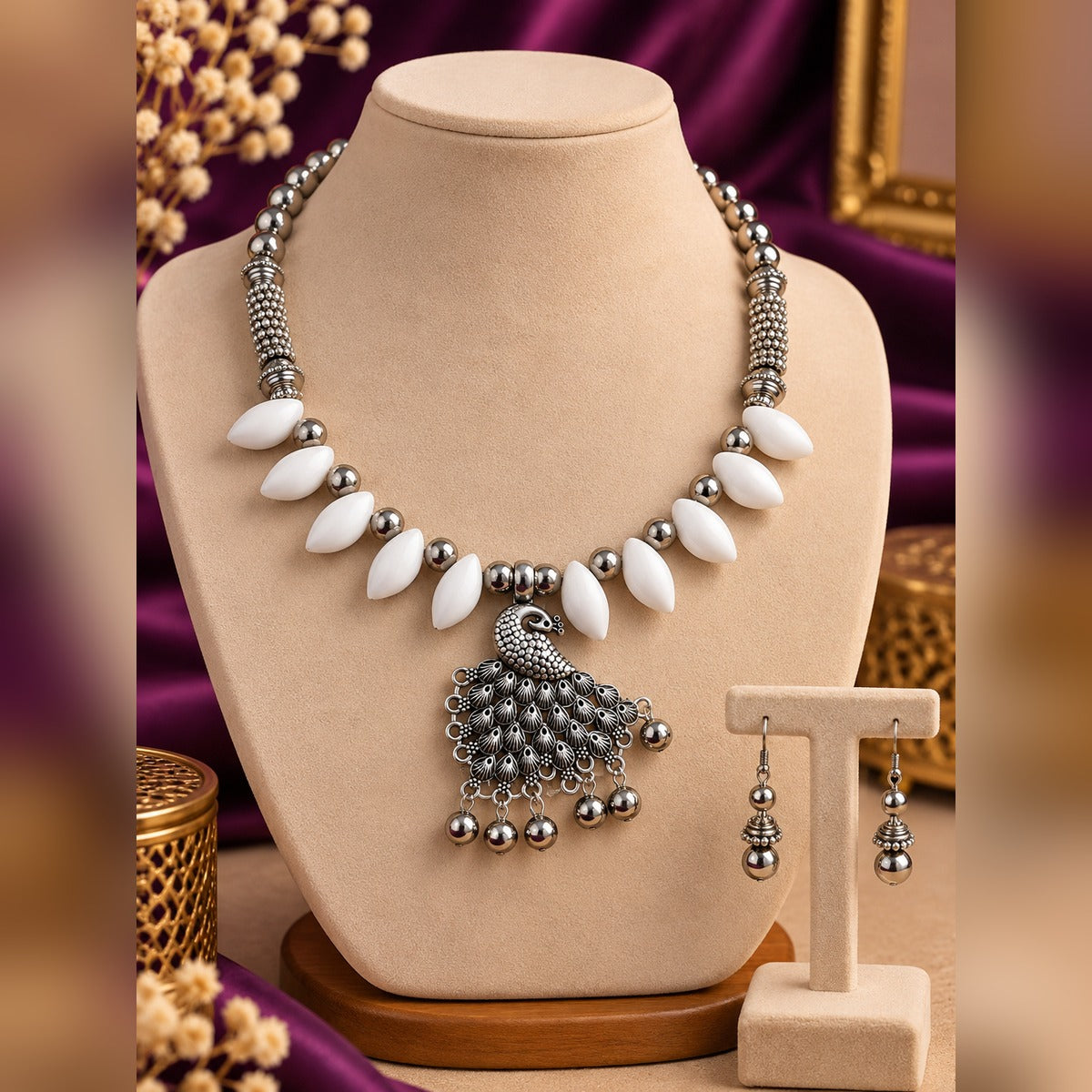 Oxidized silver peacock pendant necklace with white oval beads and silver balls, plus matching drop earrings, on a display bust