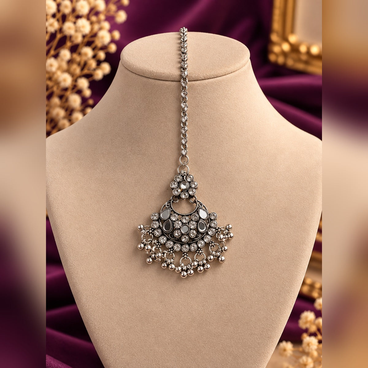 Oxidized silver maang tikka with mirror inlays, crystals and bead drops, on a display bust